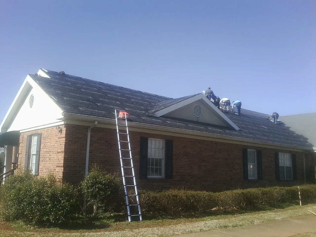 Crew tearing shingles off a brick ranch roof with a ladder set — Metal Roof Repair work by our crew in Guild