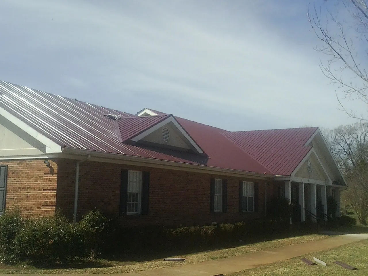 Red metal roof with gabled entries on a long brick building, from a Hail Damage Roof Repair job in Guild