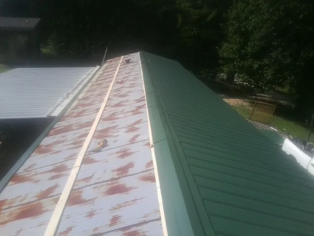 Old rusted panels beside newly installed green metal roofing — Wind Damage Roof Repair by Roofing Brothers in Guild