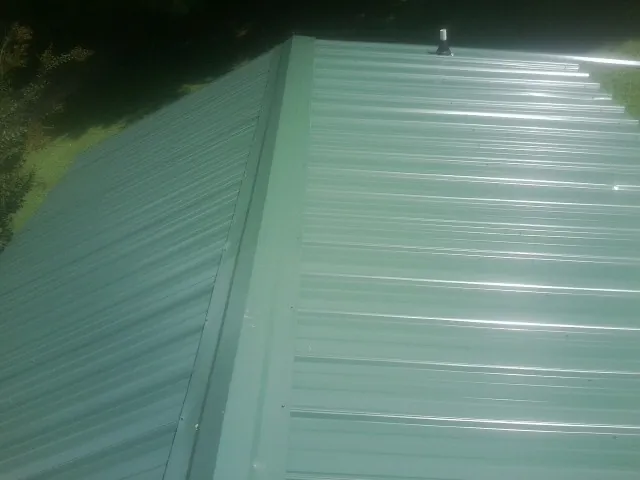 New green metal panels meeting at the ridge of a roof — Flat Roof Repair work by our crew in Guild