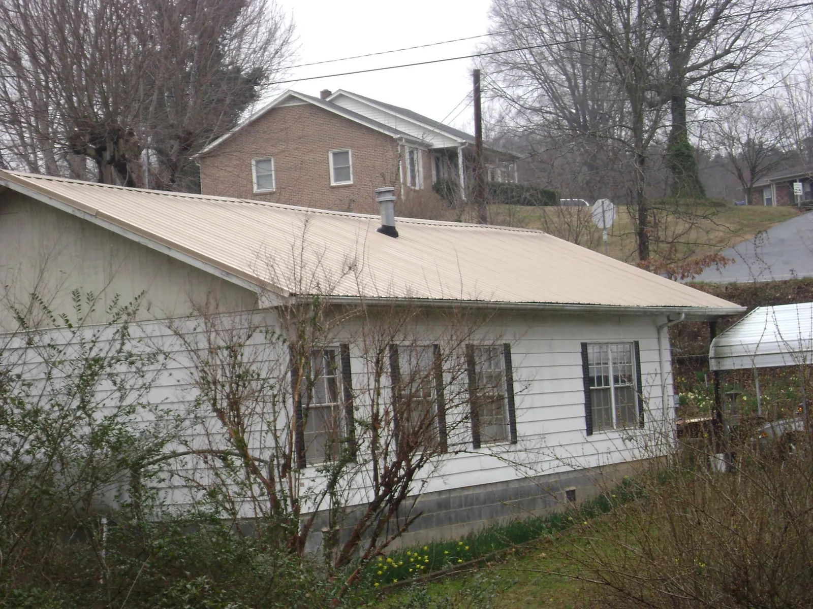 Tan metal roof on a white sided house set into a hillside — Commercial Roofing by Roofing Brothers in Guild