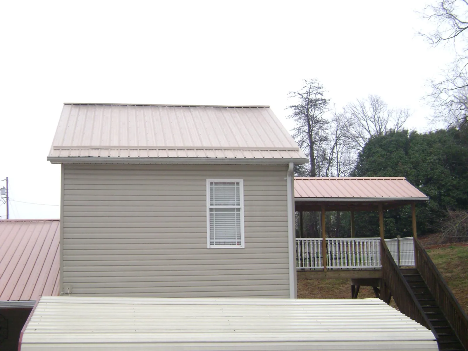 Tan metal roofs on a two story addition and attached porch, from a Roof Replacement job in Guild